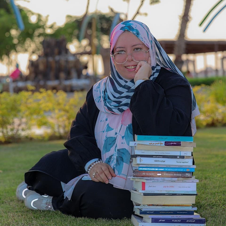 امرأة تجلس في حديقة وتضع مرفقها على مجمعة كتب للتعبير عن السعادة بكتابة ونشر الكتب